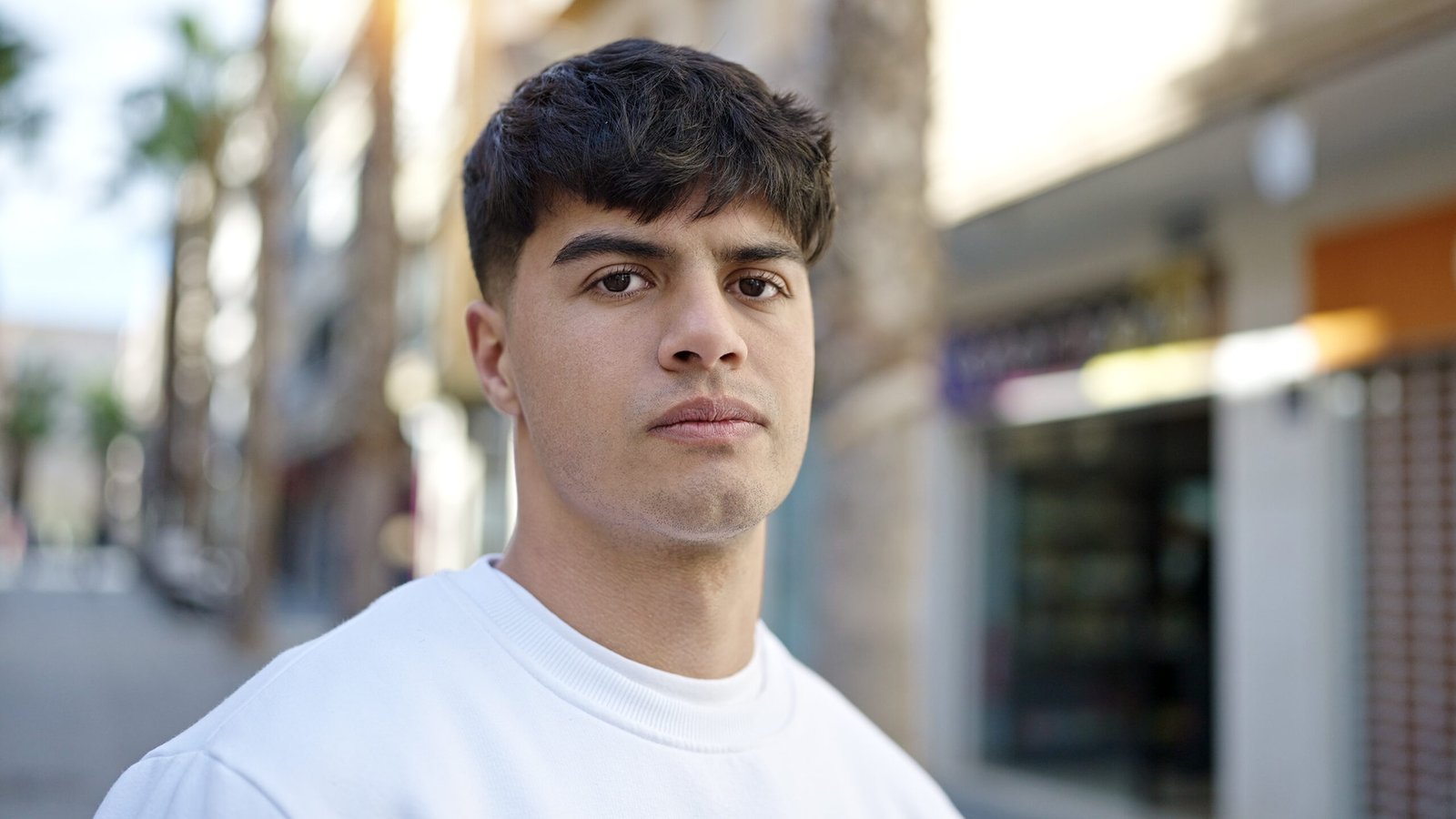 young hispanic man standing with serious expression at street